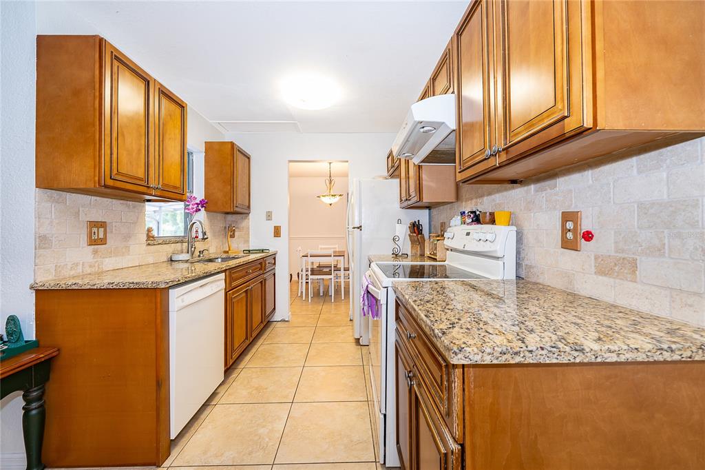 A kitchen with wood cabinets, granite countertops, tile backsplash, and tile flooring — 103 KILKENNY COURT, LONGWOOD, FL