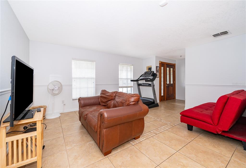 A living room features tile flooring, a brown leather sofa, a red futon, and a treadmill — 103 KILKENNY COURT, LONGWOOD, FL