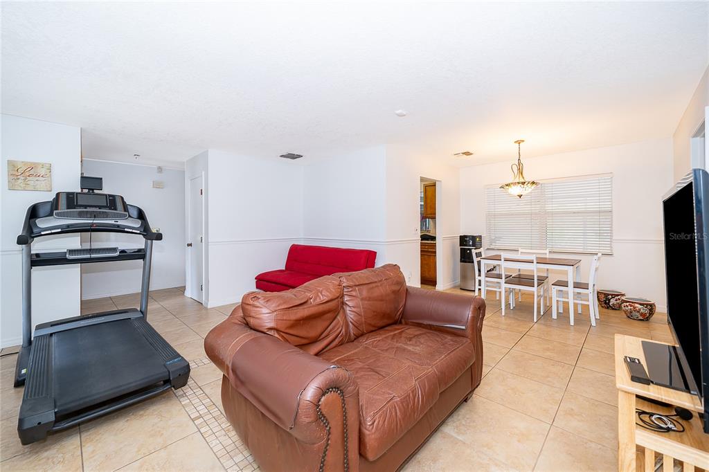 A living room with tile floors, a treadmill, a brown leather sofa, and a dining area — 103 KILKENNY COURT, LONGWOOD, FL