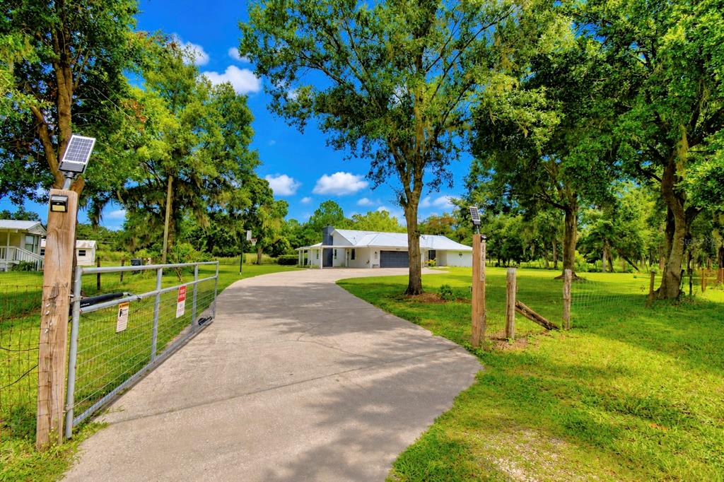 A concrete driveway leads through a gated entrance toward a white house among trees — 8610 STATE ROAD 33 N, LAKELAND, FL