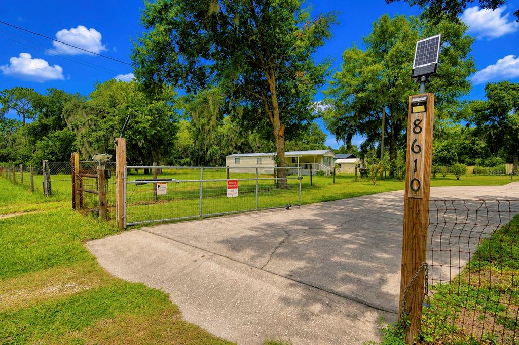 A gated driveway leads to a mobile home on a grassy lot with mature trees — 8610 STATE ROAD 33 N, LAKELAND, FL