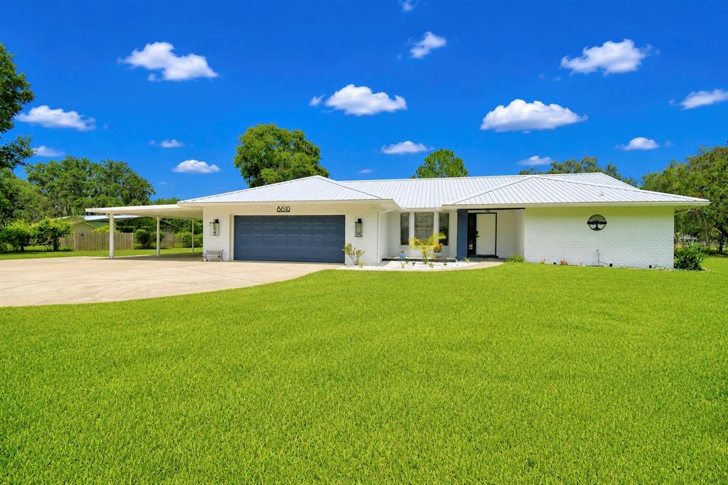 A white brick ranch-style house features a metal roof, a large garage, and a carport — 8610 STATE ROAD 33 N, LAKELAND, FL