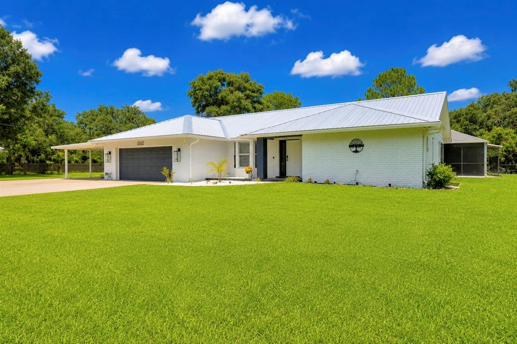 A white brick house with a metal roof and an attached garage sits on a lawn — 8610 STATE ROAD 33 N, LAKELAND, FL