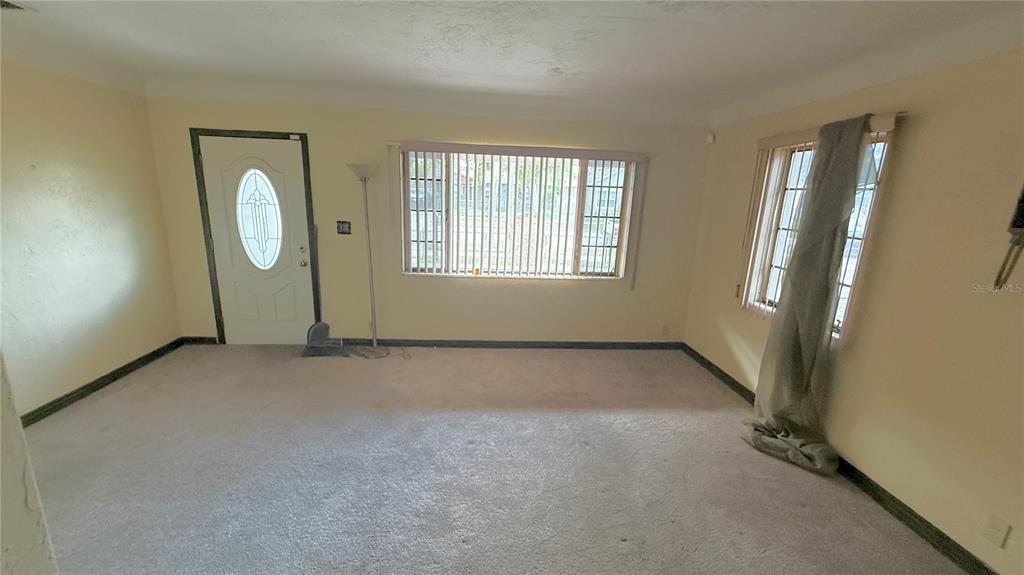 An empty living room features beige carpet, light yellow walls, and two windows with blinds — 2055 29TH STREET S, ST PETERSBURG, FL