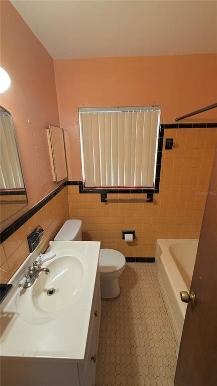 A bathroom features a white vanity, a toilet, and a bathtub with yellow wall tiles — 2055 29TH STREET S, ST PETERSBURG, FL