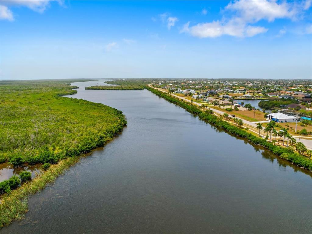 An aerial view shows a waterway separating a dense green forest from a residential neighborhood — 14159 ONSLOW LANE, PORT CHARLOTTE, FL