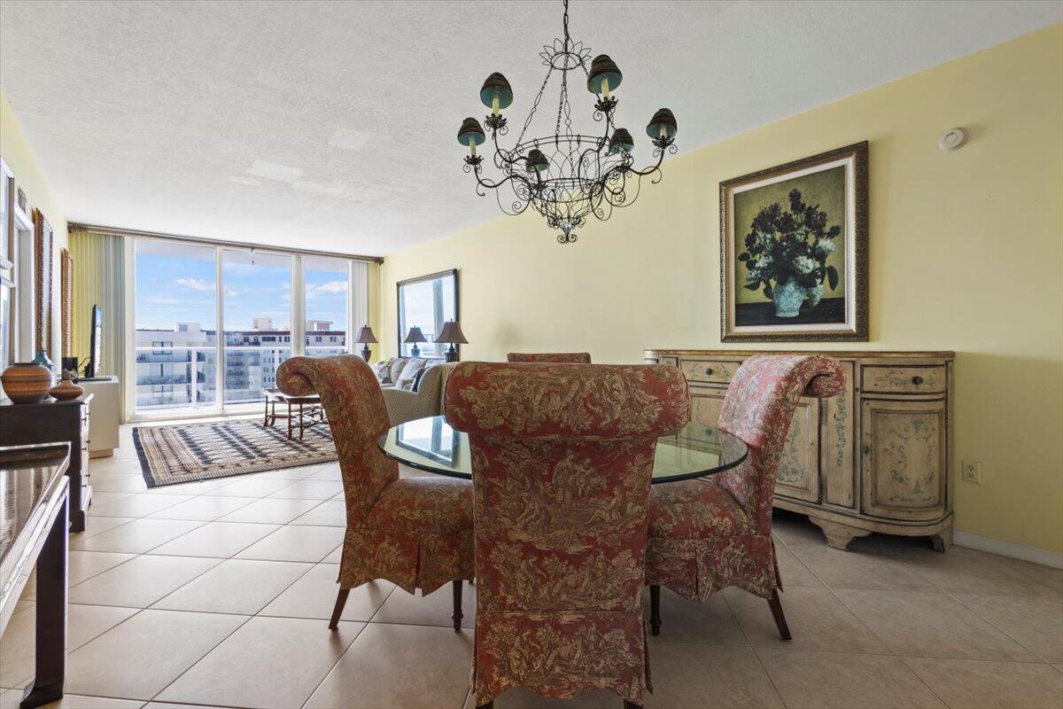 A dining area features a glass-topped table, patterned chairs, a chandelier, and a sideboard — 3450 S Ocean Boulevard # 8120, Palm Beach FL 33480, PALM BEACH, FL