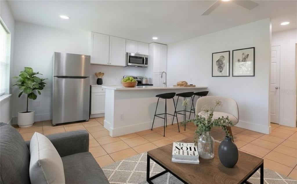 A modern kitchen with white cabinets and stainless steel appliances overlooks a furnished living area — 3017 49TH STREET S UNIT 5, GULFPORT, FL
