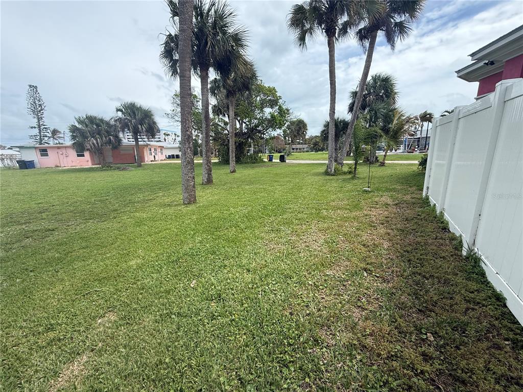 A grassy backyard features several palm trees and a white vinyl privacy fence — CORAL CIRCLE, HUTCHINSON ISLAND, FL