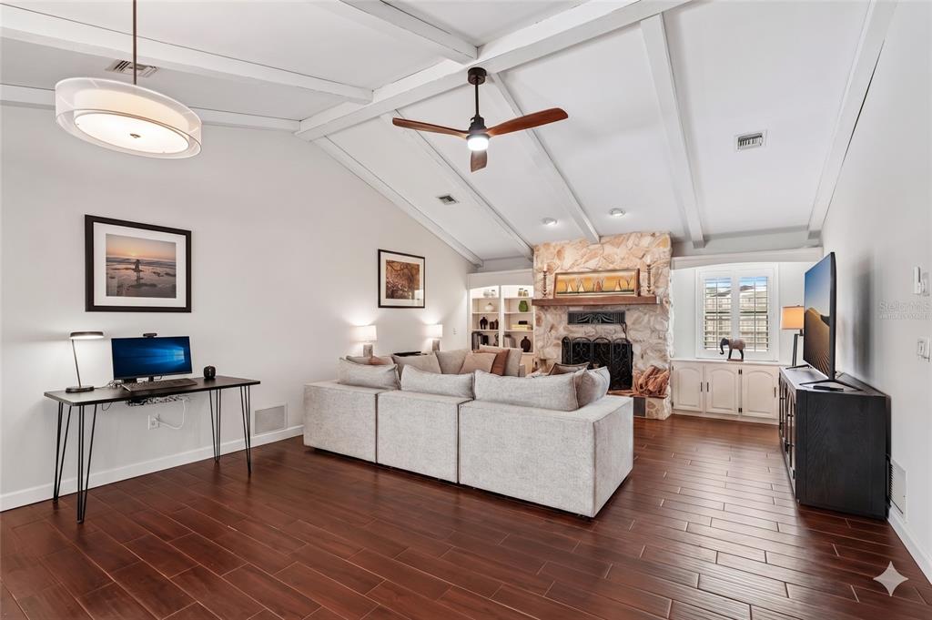 A living room features a stone fireplace, vaulted beamed ceilings, and dark wood-look tile flooring — 1201 JAMAICA ROAD, VENICE, FL