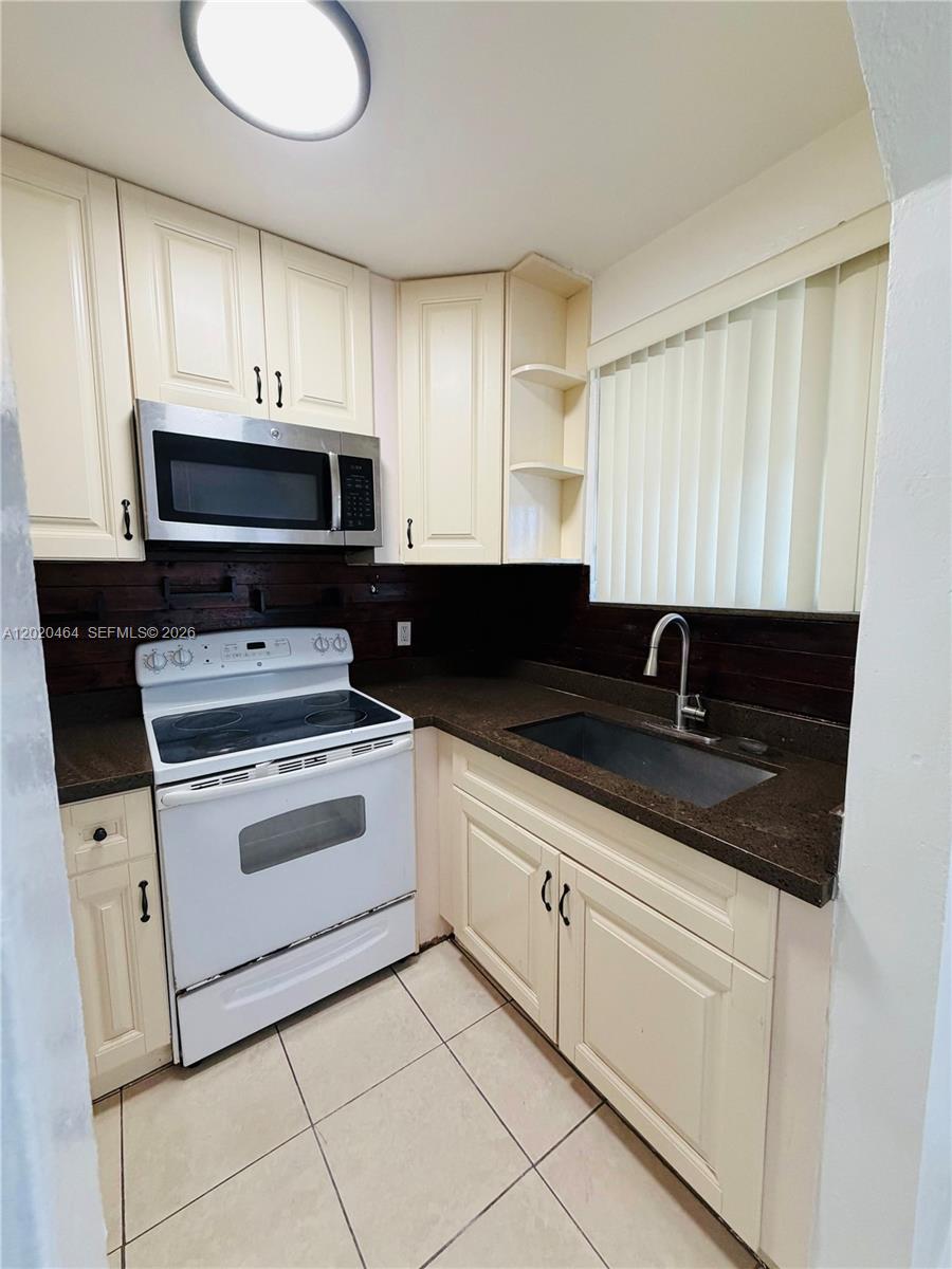 A kitchen features cream-colored cabinets, dark countertops, a white stove, and a dark backsplash — 756 N 17th Ave # 15, Hollywood FL 33020, HOLLYWOOD, FL