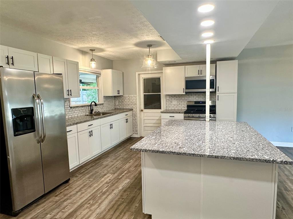 A kitchen features white cabinets, granite countertops, stainless steel appliances, and a central island — 5936 ELM STREET, NEW PORT RICHEY, FL