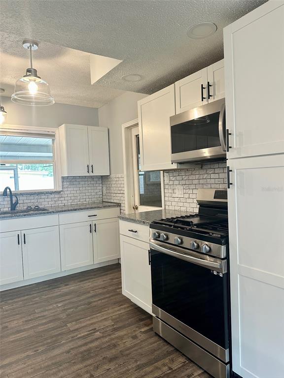 A kitchen features white cabinets, stainless steel appliances, a subway tile backsplash, and wood-look flooring — 5936 ELM STREET, NEW PORT RICHEY, FL