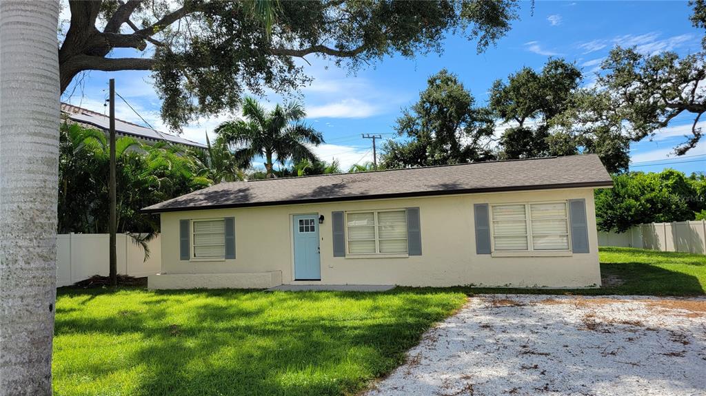 A single-story house with light-colored stucco walls, a light blue door, and a gravel driveway — 3932 SUNSHINE AVENUE, SARASOTA, FL