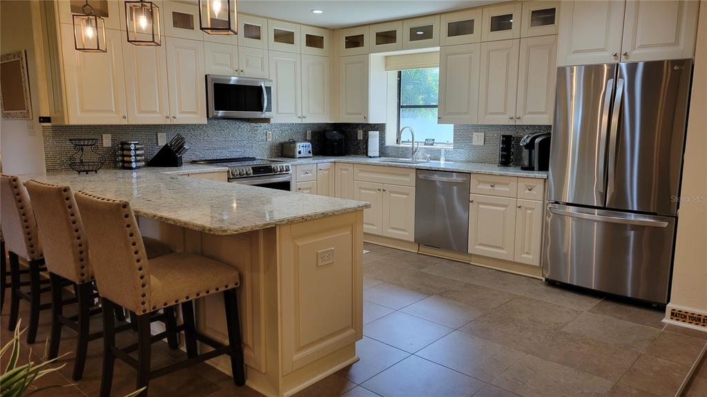 A kitchen features cream-colored cabinets, granite countertops, stainless steel appliances, and a breakfast bar — 3932 SUNSHINE AVENUE, SARASOTA, FL