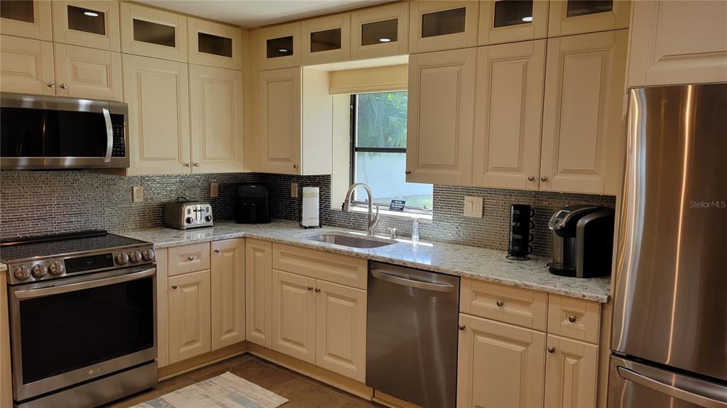 A kitchen features cream-colored cabinets, stainless steel appliances, and a tiled backsplash — 3932 SUNSHINE AVENUE, SARASOTA, FL