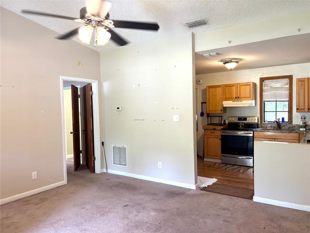 A living room with carpeted flooring leads into a kitchen with wooden cabinets and appliances — 333 RIVIERA DRIVE, CRESCENT CITY, FL