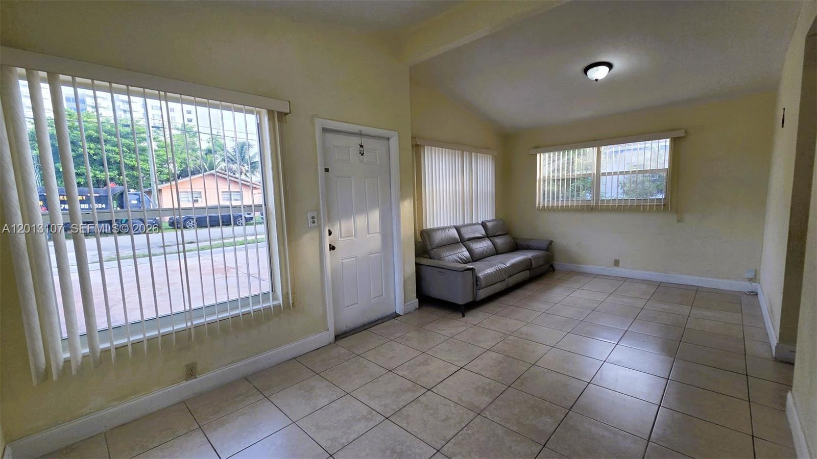 A living room features light-colored tile floors, yellow walls, vertical blinds, and a gray sofa — 2335 NW 55th St, Miami FL 33142, MIAMI, FL