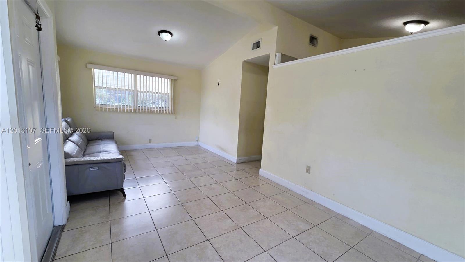 A living room features light-colored tile flooring, pale yellow walls, and a grey leather sofa — 2335 NW 55th St, Miami FL 33142, MIAMI, FL
