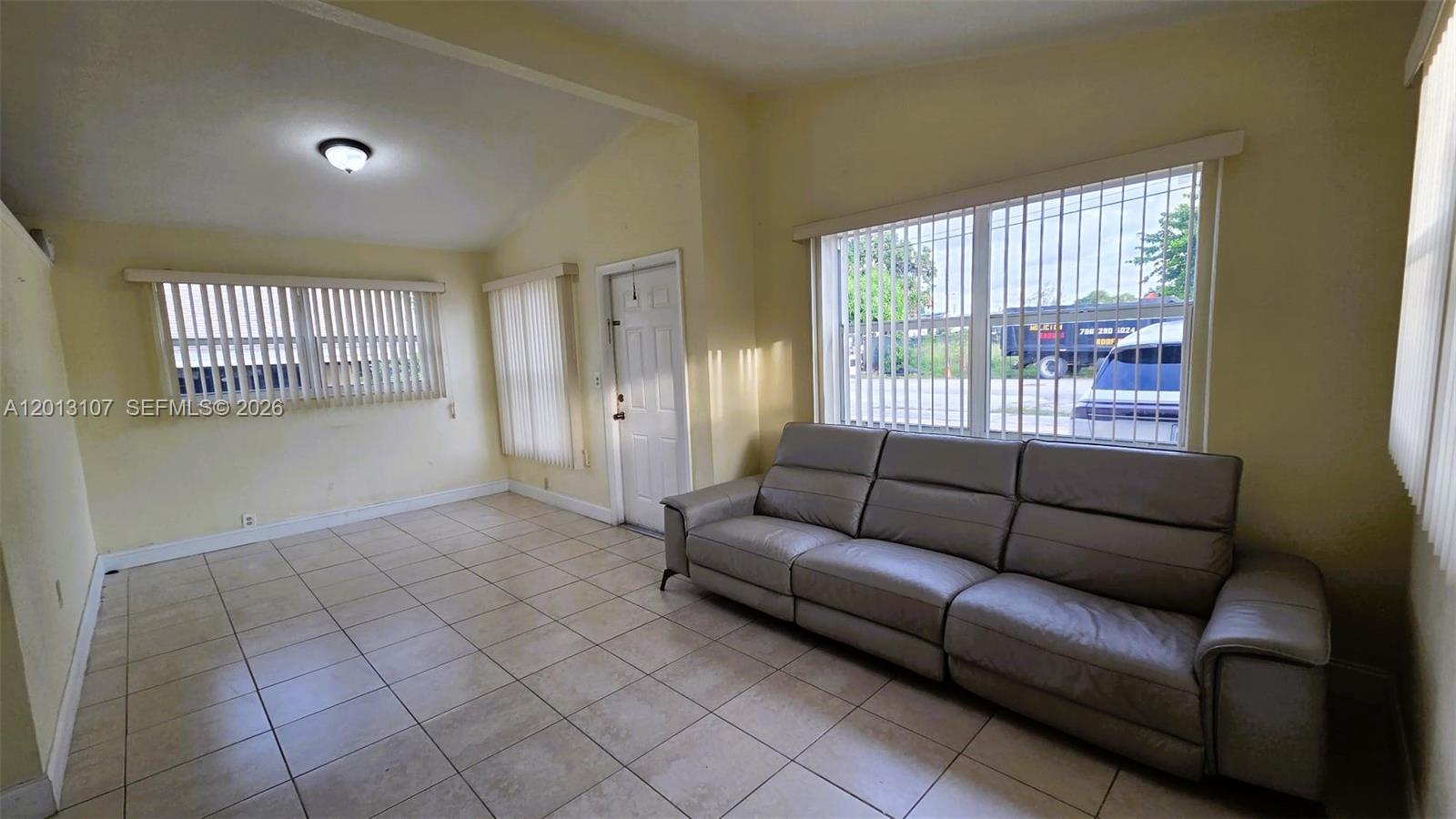A living room features light tile flooring, a gray leather sofa, and large windows — 2335 NW 55th St, Miami FL 33142, MIAMI, FL