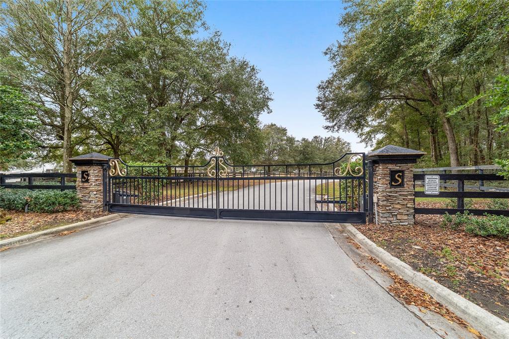 A black metal gate with stone pillars marks the entrance to a tree-lined driveway — 6208 NW 12TH STREET, OCALA, FL
