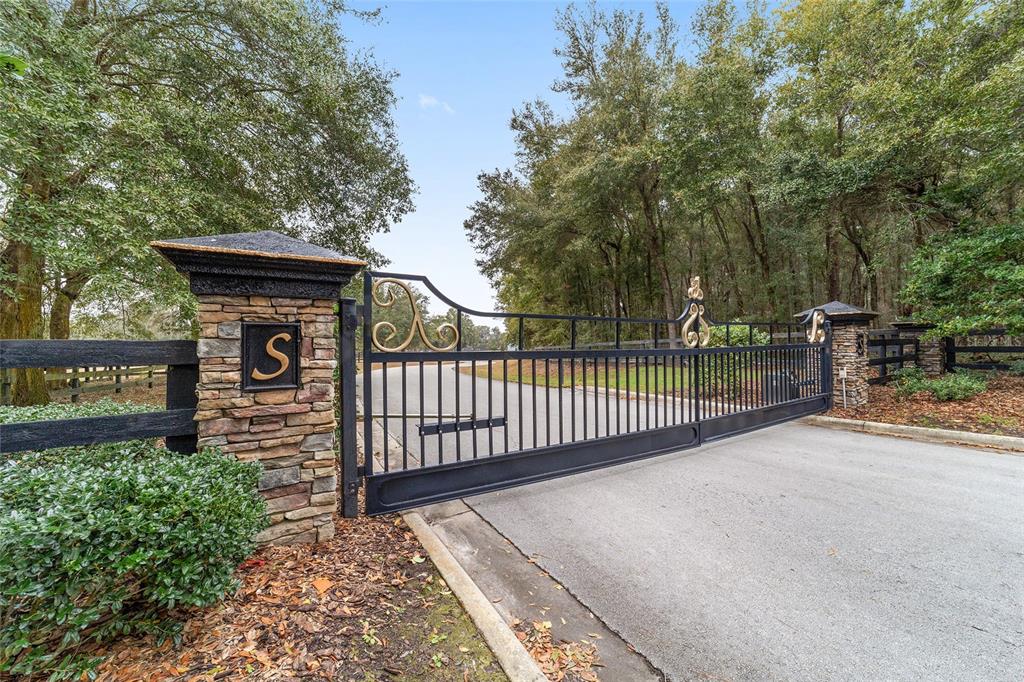A black metal gate with stone pillars marks the entrance to a wooded property — 6208 NW 12TH STREET, OCALA, FL