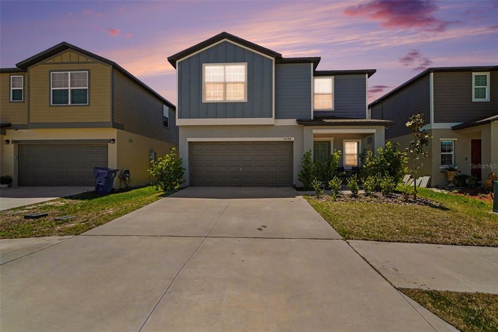 A two-story suburban house with a concrete driveway, garage, and blue siding at sunset — 35194 ACKLEY TRACE, ZEPHYRHILLS, FL