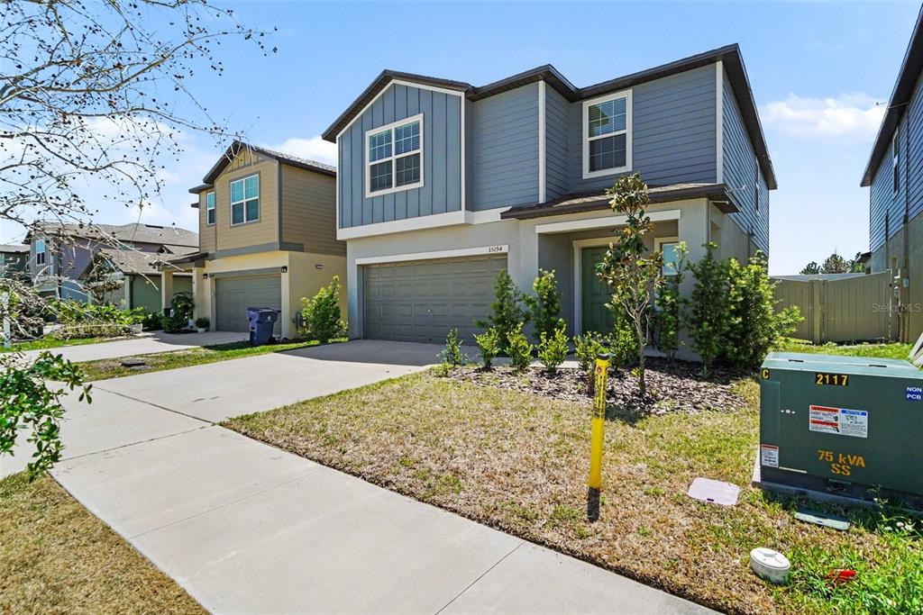 A two-story house with blue siding, a two-car garage, and a green electrical transformer box — 35194 ACKLEY TRACE, ZEPHYRHILLS, FL