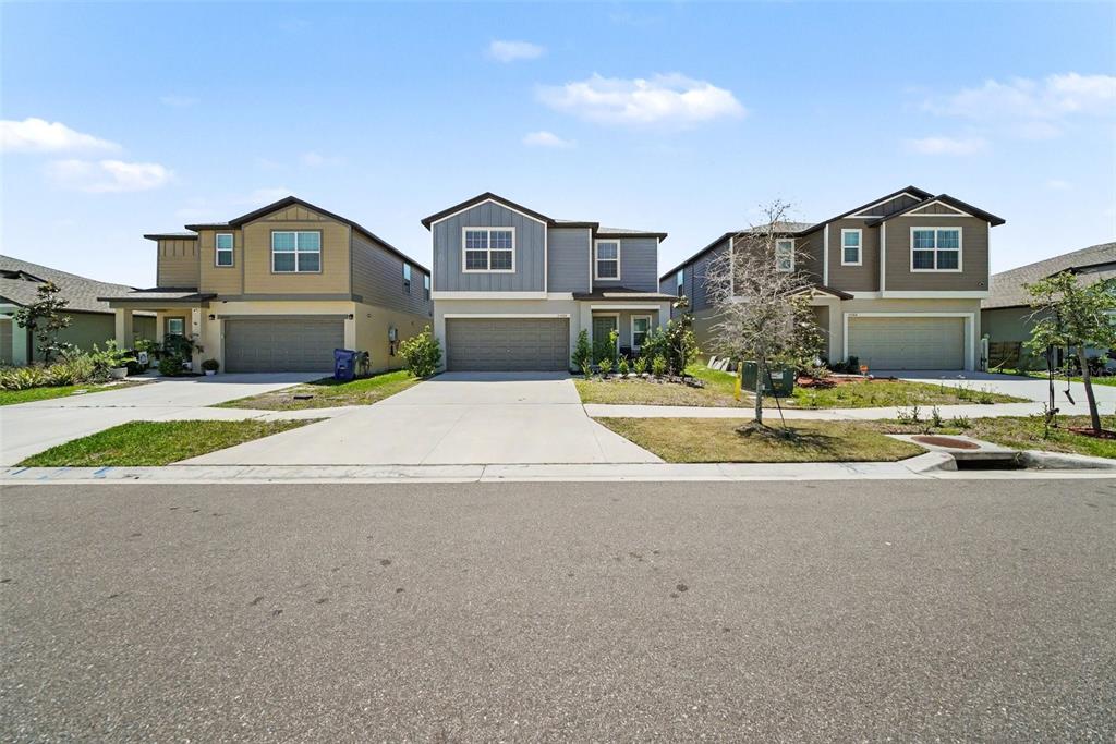Three suburban two-story houses with driveways and garages stand side-by-side under a blue sky — 35194 ACKLEY TRACE, ZEPHYRHILLS, FL