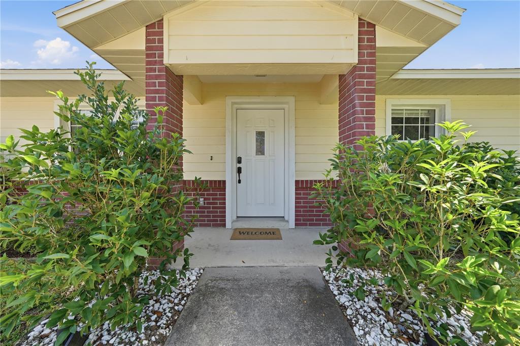 A front entrance with a white door, brick pillars, and landscaping on a concrete walkway — 3835 NE 13TH AVENUE, OCALA, FL