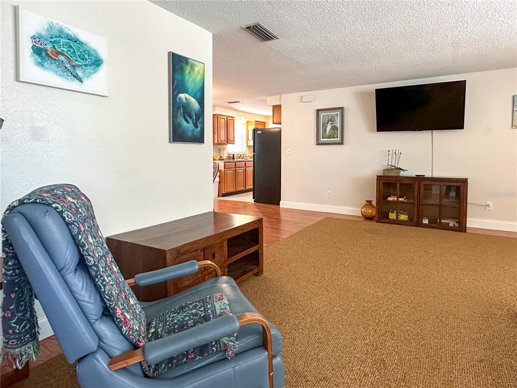 A living room features a blue recliner, a television, and a view into the kitchen — 5008 27TH AVENUE W, BRADENTON, FL