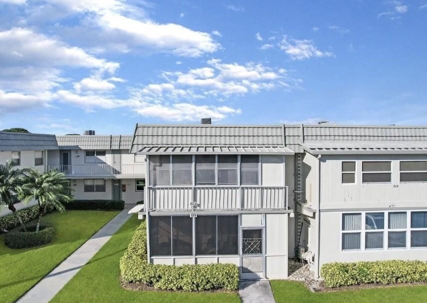 Exterior view of a two-story apartment building with screened balconies and a grassy lawn — 223 Flanders, Delray Beach FL 33484, DELRAY BEACH, FL