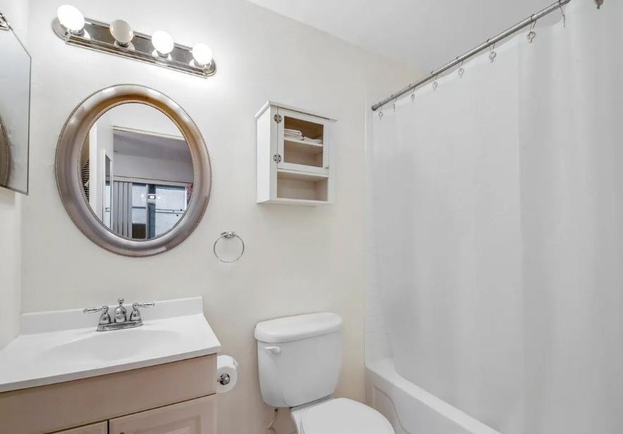 A bathroom features a vanity with a round mirror, a toilet, and a shower-tub combo — 223 Flanders, Delray Beach FL 33484, DELRAY BEACH, FL
