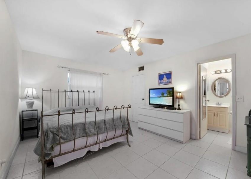 A bedroom with a metal bed frame, white dresser, ceiling fan, and an attached bathroom — 223 Flanders, Delray Beach FL 33484, DELRAY BEACH, FL