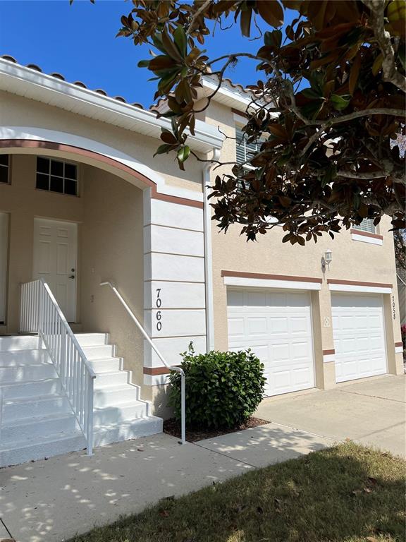 A two-story stucco townhouse features a white front door, stairs, and two garage doors — 7060 STRAND CIRCLE UNIT 7060, BRADENTON, FL