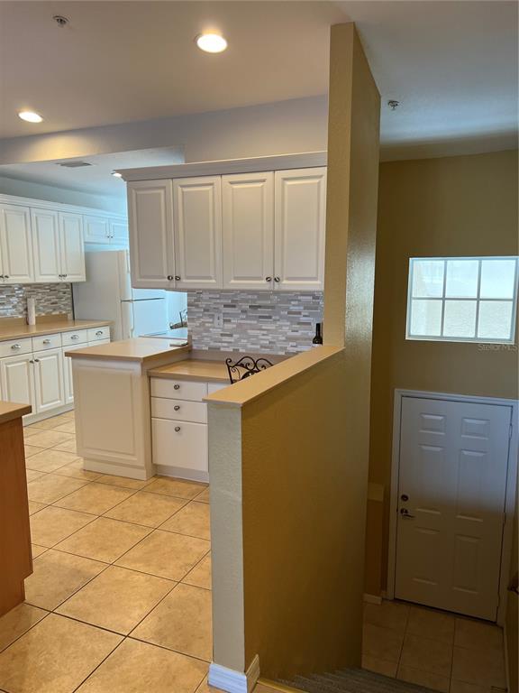 A kitchen with white cabinets and tile flooring overlooks a staircase and an entry door — 7060 STRAND CIRCLE UNIT 7060, BRADENTON, FL
