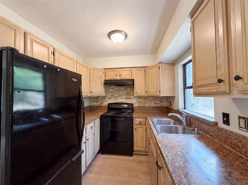 A kitchen with light wood cabinets, black appliances, a stone backsplash, and laminate countertops — 2630 SE 8TH AVENUE, OCALA, FL