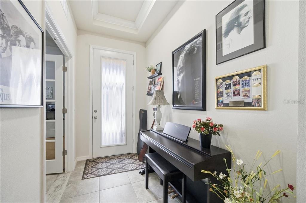 An entryway features a digital piano, framed music memorabilia, and a glass-paneled front door — 10591 HERON HIDEAWAY LOOP, LAND O LAKES, FL