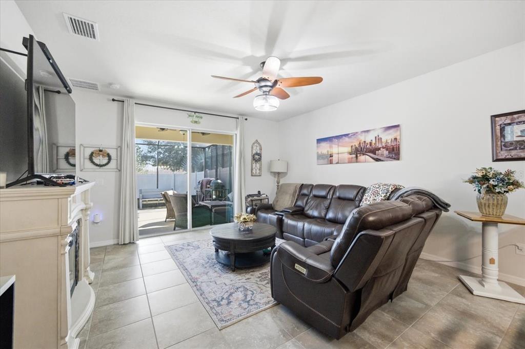A living room features tile floors, a brown leather sectional, and a sliding glass door — 10591 HERON HIDEAWAY LOOP, LAND O LAKES, FL