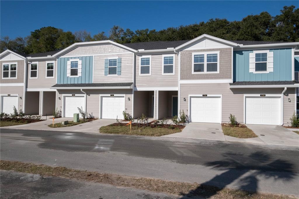 A row of modern townhomes with light-colored siding, blue accents, and attached garages — 704 NW 126TH TERRACE, NEWBERRY, FL