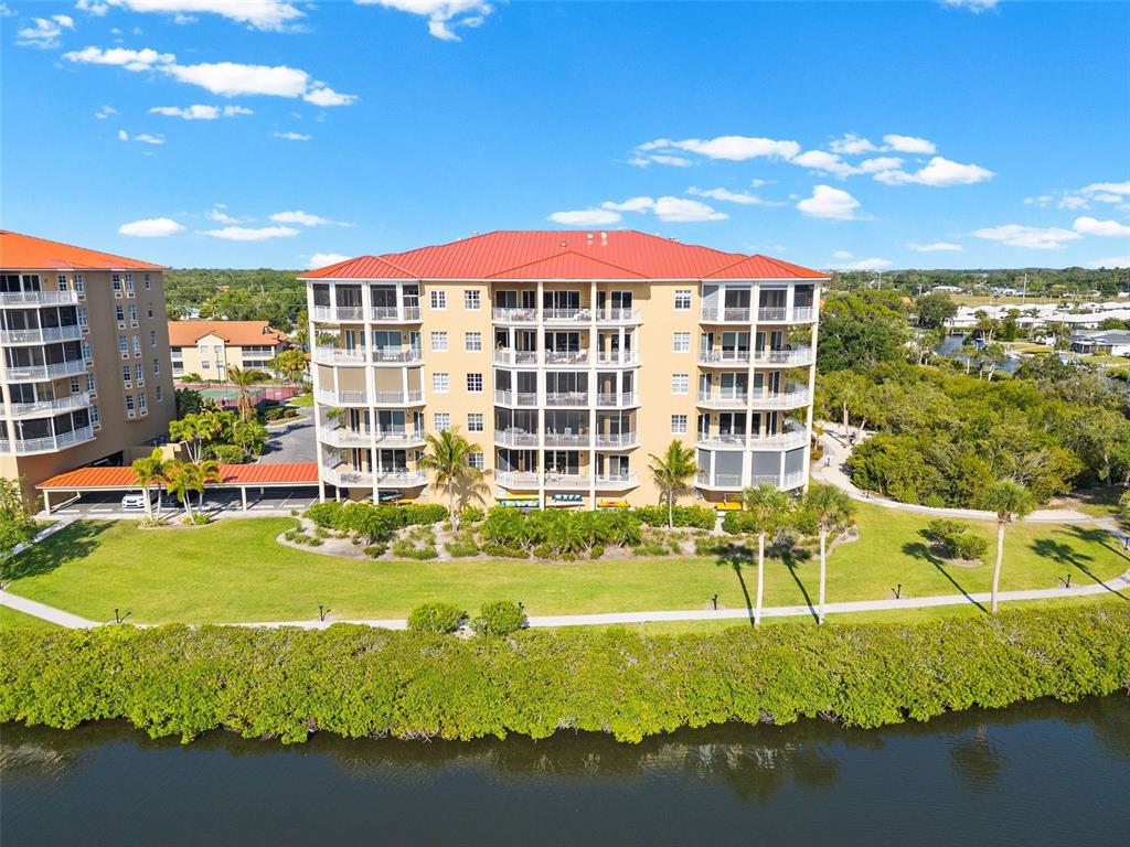 An exterior view of a multi-story apartment building with a red roof near water — 6100 JESSIE HARBOR DRIVE UNIT 202, OSPREY, FL