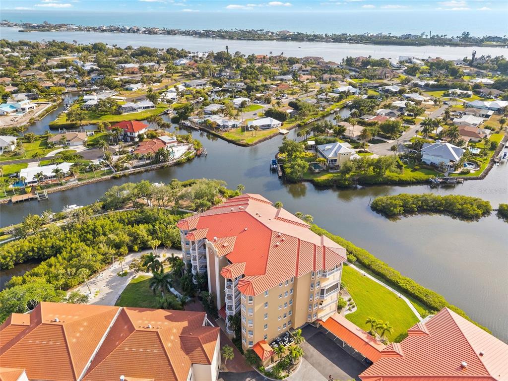 An aerial view shows a multi-story building with a red roof surrounded by waterways — 6100 JESSIE HARBOR DRIVE UNIT 202, OSPREY, FL