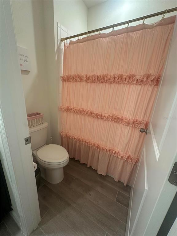 A bathroom features a toilet, wood-look tile flooring, and a ruffled peach shower curtain — 1169 NW 133RD WAY, NEWBERRY, FL