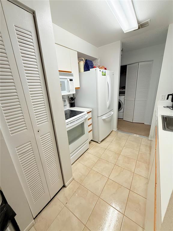 A galley-style kitchen features white appliances, light-colored tile flooring, and louvered closet doors — 3001 58TH AVENUE S UNIT 1002, ST PETERSBURG, FL