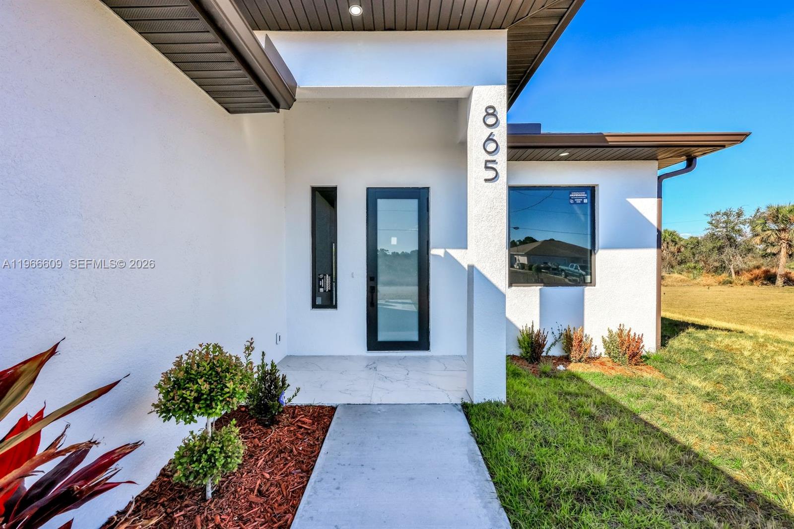 The exterior of a modern white house features a glass front door and address numbers — 865 Chipley ST E, Lehigh Acres FL 33974, LEHIGH ACRES, FL