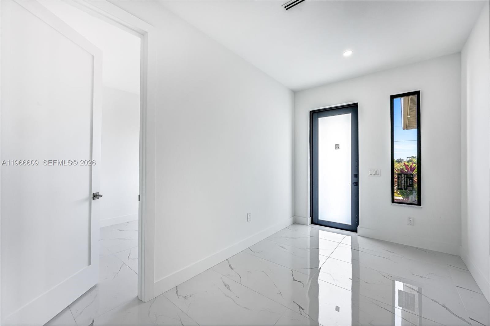 A minimalist entryway features white walls, marble-patterned tile floors, a glass-paneled door, and a window — 865 Chipley ST E, Lehigh Acres FL 33974, LEHIGH ACRES, FL