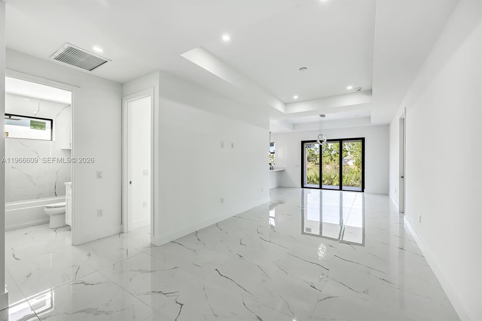 A bright, minimalist room features white marble-look tile flooring and a view of greenery — 865 Chipley ST E, Lehigh Acres FL 33974, LEHIGH ACRES, FL