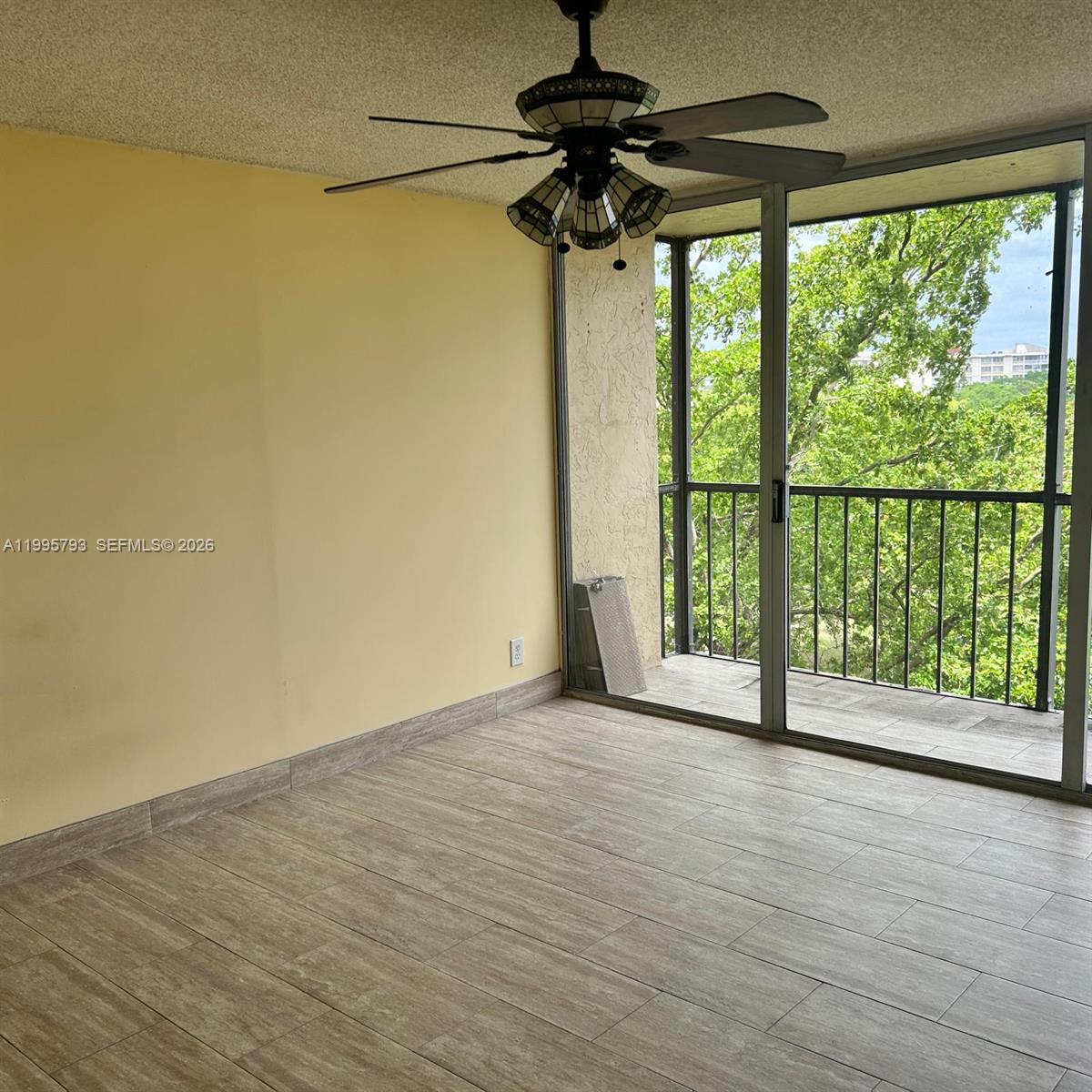 An empty room features light yellow walls, wood-look tile flooring, a ceiling fan, and a balcony — 3771 Environ Blvd # 650, Lauderhill FL 33319, LAUDERHILL, FL