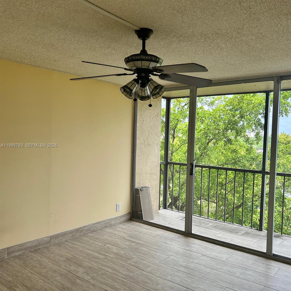 A sunroom features a stained-glass ceiling fan, light-colored walls, wood-look tile flooring, and a balcony — 3771 Environ Blvd # 650, Lauderhill FL 33319, LAUDERHILL, FL