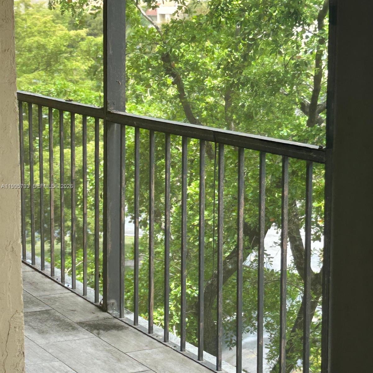 A screened-in balcony with metal railings overlooks lush green trees — 3771 Environ Blvd # 650, Lauderhill FL 33319, LAUDERHILL, FL